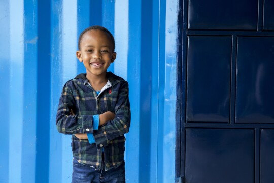 A young boy smiling in front of blue building